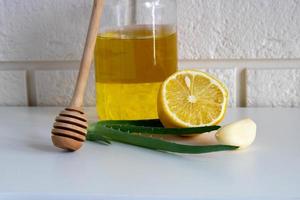 composição com remédios naturais para resfriado em uma mesa branca em um fundo de tijolo. alho, mel, limão, remédios populares de aloe para resfriados de outono, covida foto