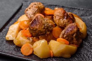 ensopado de carne e legumes em um prato preto com batatas assadas foto