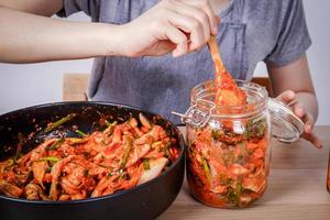 mulher asiática sentada e fazendo kimchi ela está usando luvas de proteção e um chapéu. para manter os alimentos limpos. conceito de comida fermentada coreana de fundo branco feito de vegetais. foto