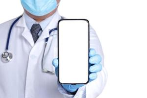 médico usando uma máscara cirúrgica usando luvas azuis. segure o smartphone com uma tela branca. conectar-se à comunicação através da tecnologia online. os médicos podem examinar os pacientes por meio de videochamadas. foto
