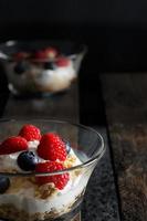 framboesas, mirtilos, cereais e iogurte em uma tigela de vidro em tábuas de madeira velhas. pequeno-almoço saudável para uma vida saudável. imagem vertical. foto