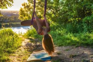 uma jovem ginasta está envolvida em ioga aérea na natureza no parque, usando uma combinação de poses tradicionais de ioga, pilates e dança suave foto