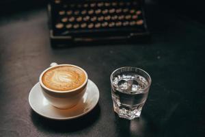uma xícara de café com leite em uma xícara de cerâmica e um copo de água foto