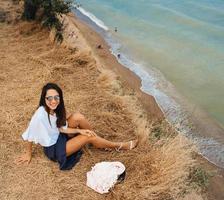 mulher atraente em saia de verão e camisa senta-se na praia foto