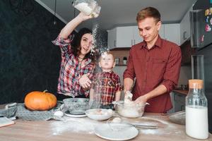 pai, mãe e filho pequeno cozinham uma torta foto