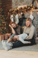 jovem família caucasiana mãe pai filho perto da lareira árvore de natal foto