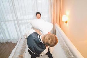 luta de travesseiros dos noivos em um quarto de hotel foto