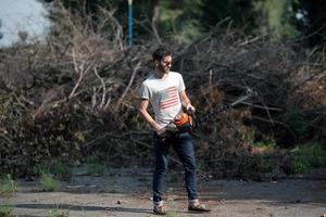 o homem de botas autênticas e jeans de ourela com uma motosserra no fundo dos galhos foto