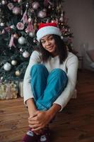 linda mulher afro-americana senta-se perto de uma árvore de natal foto