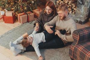 jovem família caucasiana mãe pai filho perto da lareira árvore de natal foto