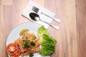 arroz frito de carne de porco e salsicha com cebola servido em um prato branco sobre uma mesa de madeira clara. foto