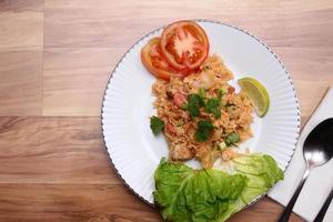 arroz frito de carne de porco e salsicha com cebola servido em um prato branco sobre uma mesa de madeira clara. foto