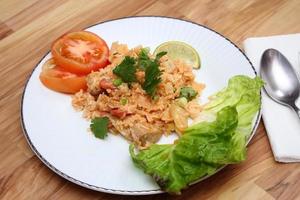 arroz frito de carne de porco e salsicha com cebola servido em um prato branco sobre uma mesa de madeira clara. foto