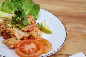 arroz frito de carne de porco e salsicha com cebola servido em um prato branco sobre uma mesa de madeira clara. foto