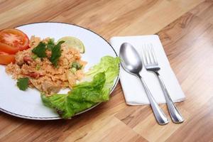 arroz frito de carne de porco e salsicha com cebola servido em um prato branco sobre uma mesa de madeira clara. foto