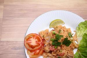 arroz frito de carne de porco e salsicha com cebola servido em um prato branco sobre uma mesa de madeira clara. foto