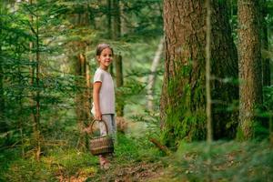 menina com uma cesta está sorrindo ao lado de uma árvore. o conceito de uma vida saudável e colher frutas na floresta foto