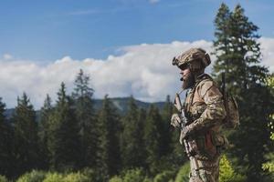 conceito de guerra. um soldado barbudo em um uniforme das forças especiais lutando contra um inimigo em uma área de floresta. foco seletivo foto