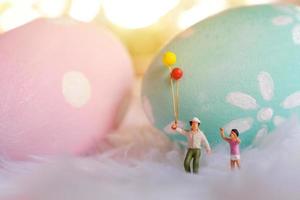 família de pessoas em miniatura segurando balão com ovos de páscoa pastel e coloridos, férias e conceito de feliz páscoa foto