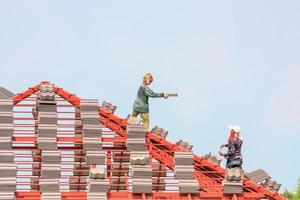 carpinteiro de construção instalando telhas no local de construção da casa foto