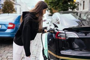 mulher perto de carro elétrico. veículo carregado na estação de carregamento. foto