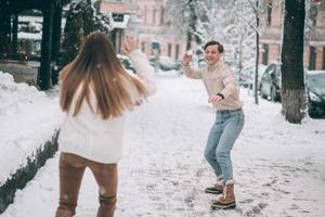 jovem casal alegre está jogando bolas de neve na rua. foto