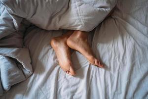 pés de mulher de close-up sozinho na cama branca foto