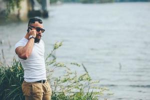 homem barbudo americano usando telefone perto do rio foto