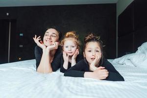 mãe e duas filhas se divertem na cama foto