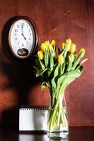 relógio de parede, calendário em branco e tulipas em vaso foto