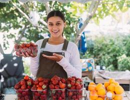 jovem vendedora positiva no trabalho, segurando morangos nas mãos foto