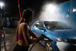 jovem mulher lavando carro azul na lavagem de carros foto