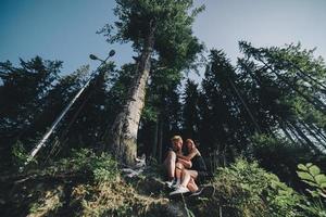 lindo casal sentado em uma floresta perto da árvore foto