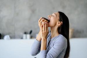 retrato de regozijo mulher come rosquinha saborosa em casa. foto