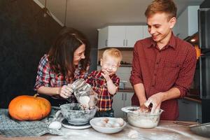 pai, mãe e filho pequeno cozinham uma torta foto