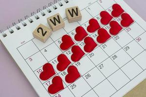 palavra 2ww no bloco de madeira com forma de coração vermelho no calendário. conceito de espera de duas semanas foto