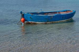 na costa do mediterrâneo encontra-se um barco de pesca de madeira azul, vazio e velho sob um céu azul foto