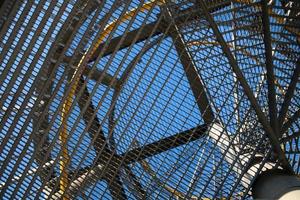 detalhe de uma escada em espiral de metal, fotografada de baixo, com vista para o céu azul.