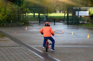 criança da escola de visão traseira aprende a andar de bicicleta no parque, retrato ao ar livre de um menino praticando como andar de bicicleta, criança no capacete andando de bicicleta pela manhã. foto