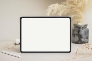 tablet tela branca vazia com maquete de lápis. flor de algodão e folhas secas na maquete de fundo bege para design foto
