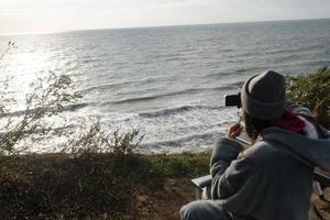 jovem tira uma foto em um smartphone da paisagem marinha