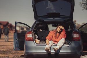 mulher jovem e atraente descansando no porta-malas de um carro foto