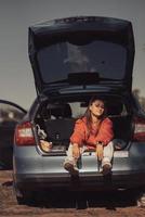 mulher jovem e atraente descansando no porta-malas de um carro foto