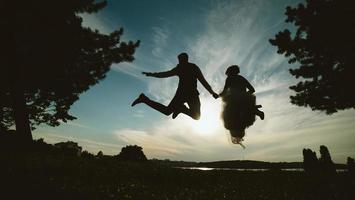 noivo e noiva pulando contra o lindo céu foto