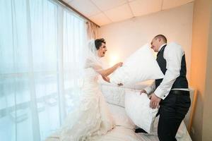 luta de travesseiros dos noivos em um quarto de hotel foto