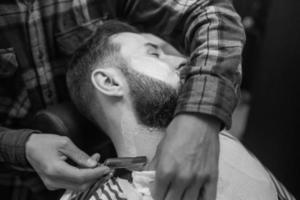 jovem barbudo sendo barbeado pelo cabeleireiro na barbearia foto