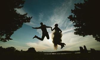 noivo e noiva pulando contra o lindo céu foto