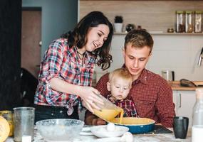 pai, mãe e filho pequeno cozinham uma torta foto