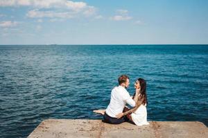 jovem casal está sentado no cais à beira-mar foto