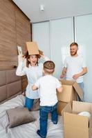 pai mãe e filho brincam no quarto com caixas de papel foto